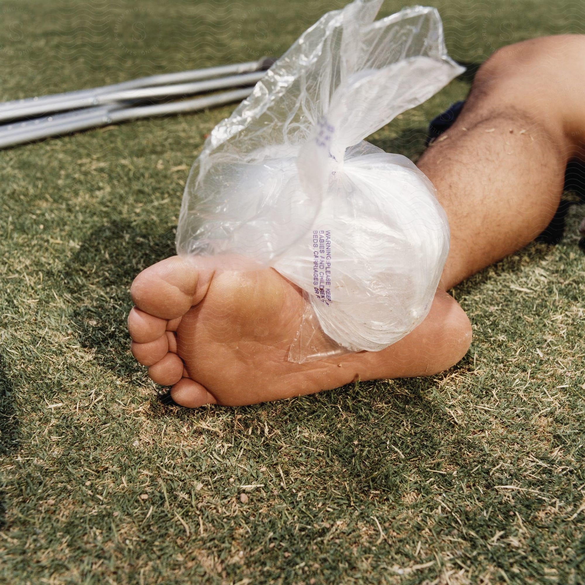 Bare foot resting on grass with an ice pack, sports equipment nearby